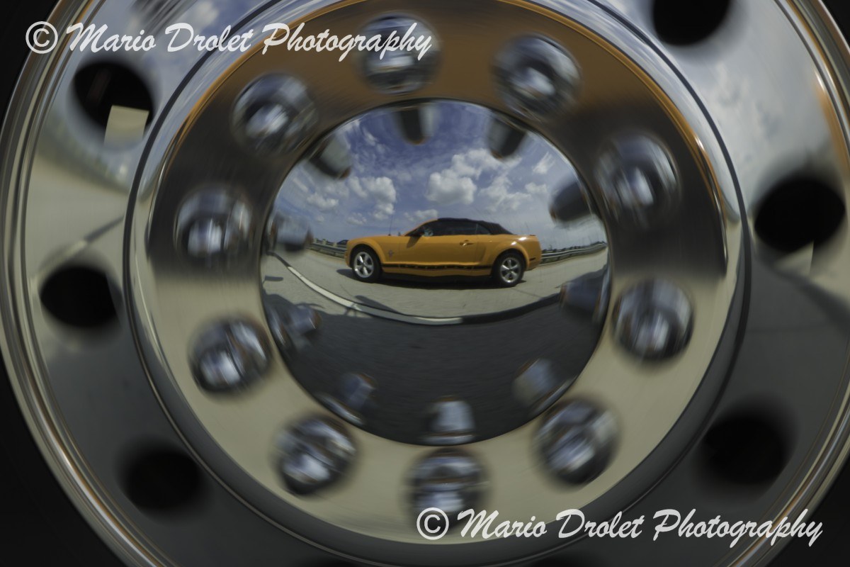 Colour photo of a car's reflection in a truck hubcap