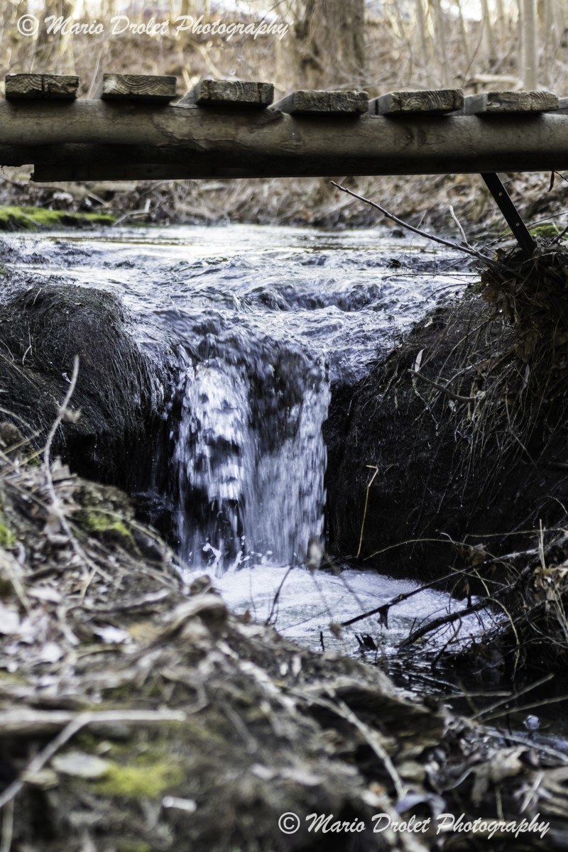 Colour photo of a small creek waterfall under a wooden bridge