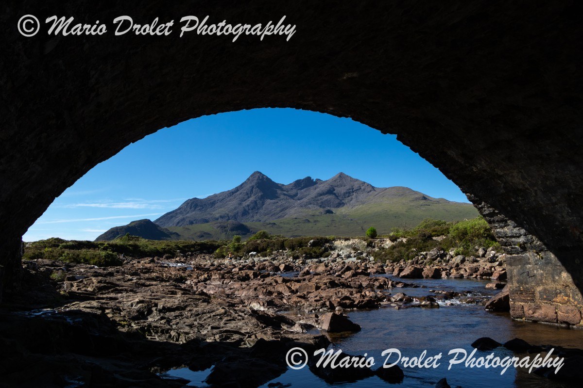 Black Cuillin ridge and landscape viewed through the arch of a bridge.